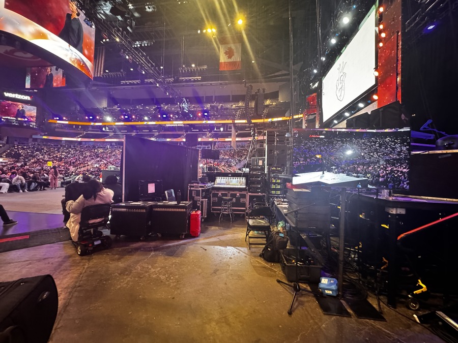 Backstage view of an LED video wall setup in a large arena, with equipment, cables, and control stations visible